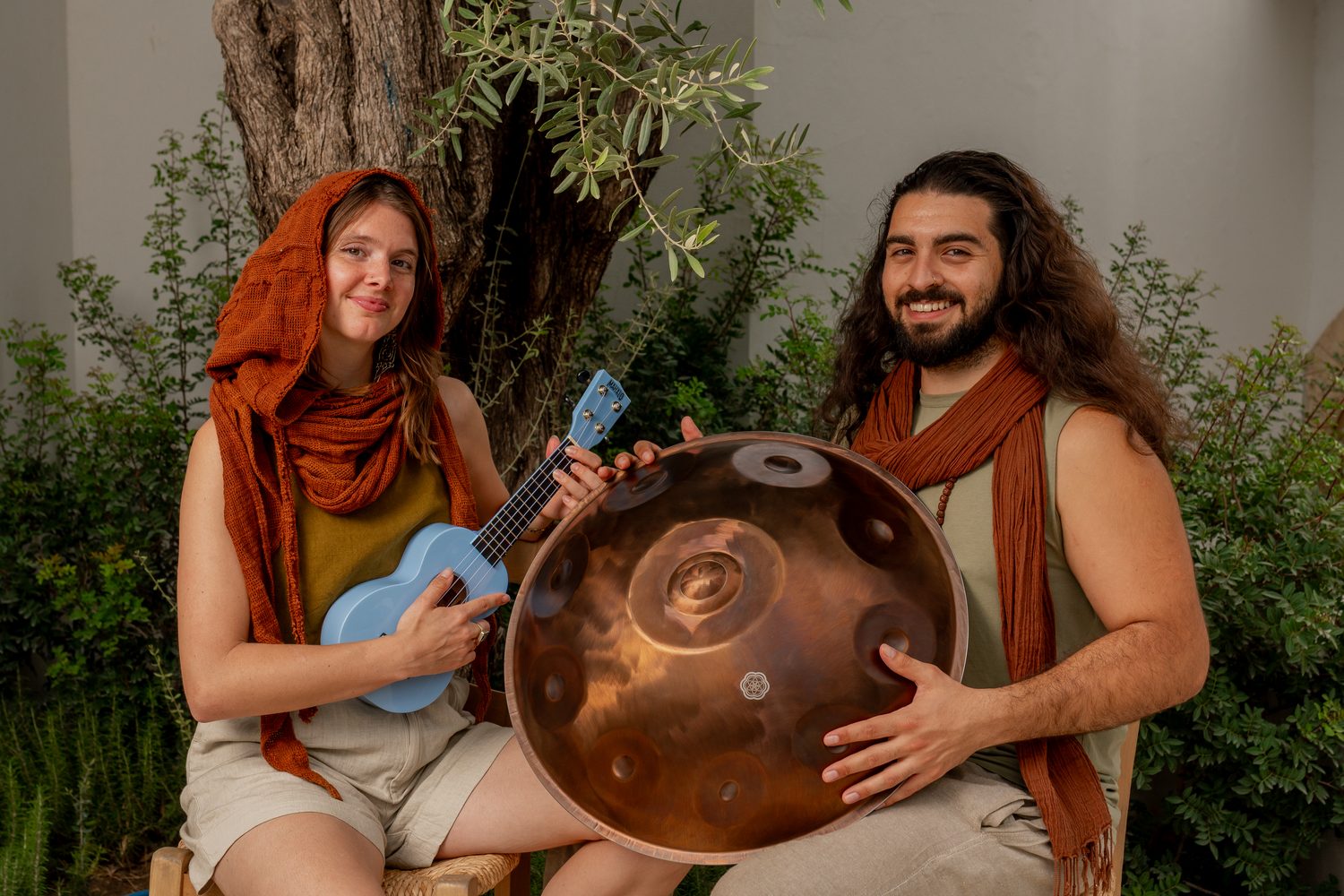Véra with a ukulele and Emre with a copper handpan under an olive tree