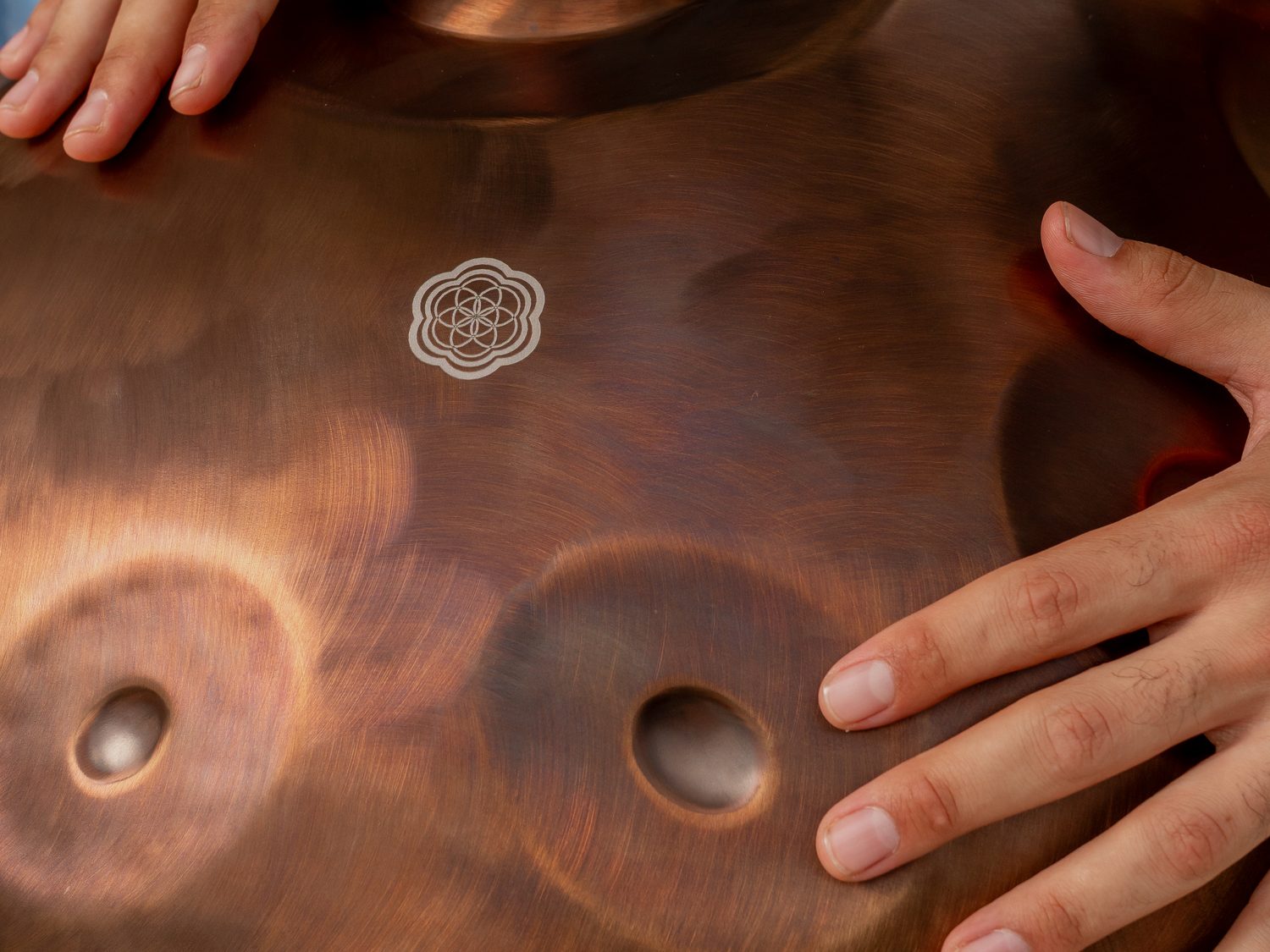 Close up of a copper VeChi Sound handpan, the seed of life logo between two hands