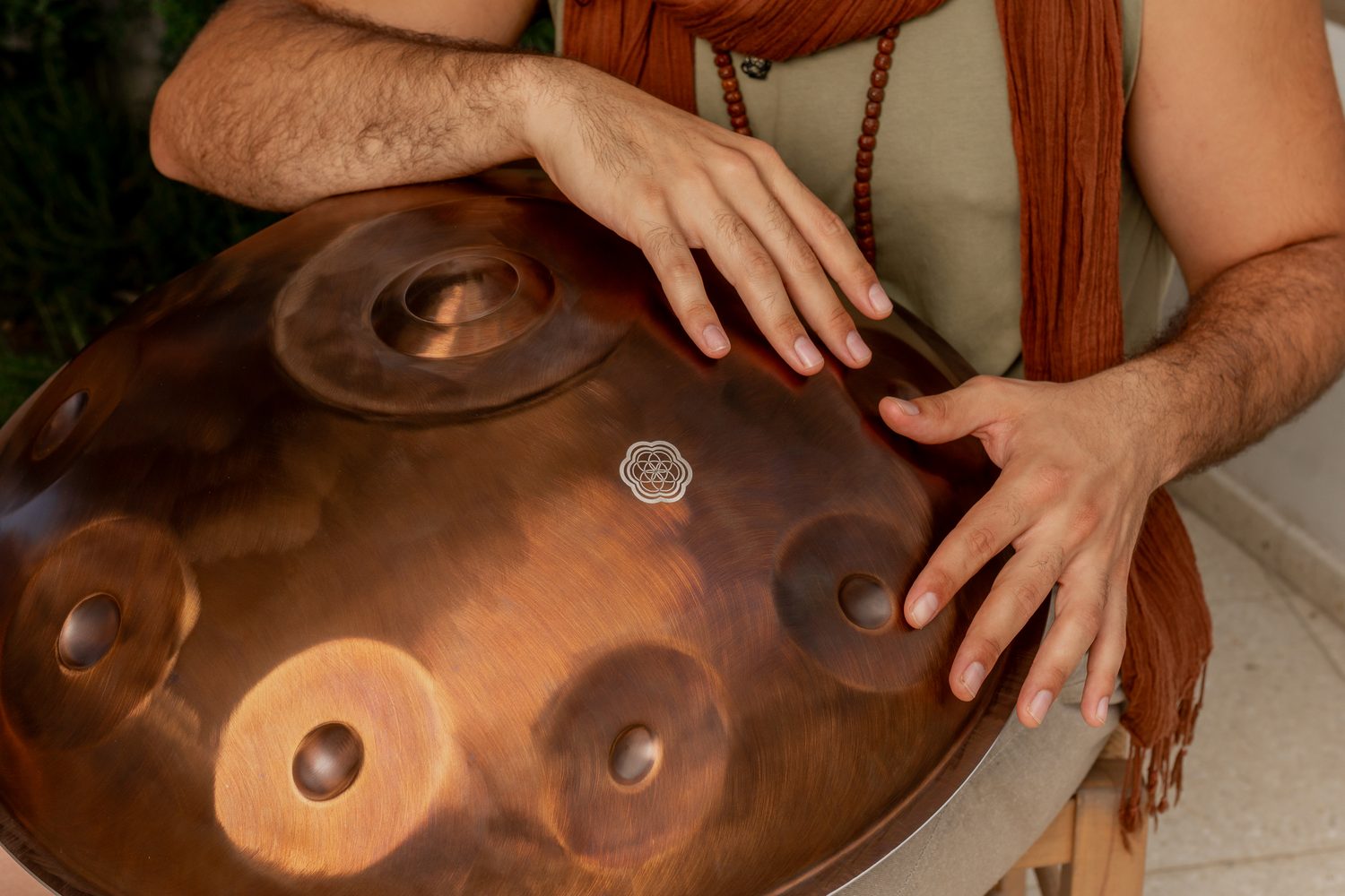 Two hands resting on the notes of a copper VeChi Sound handpan